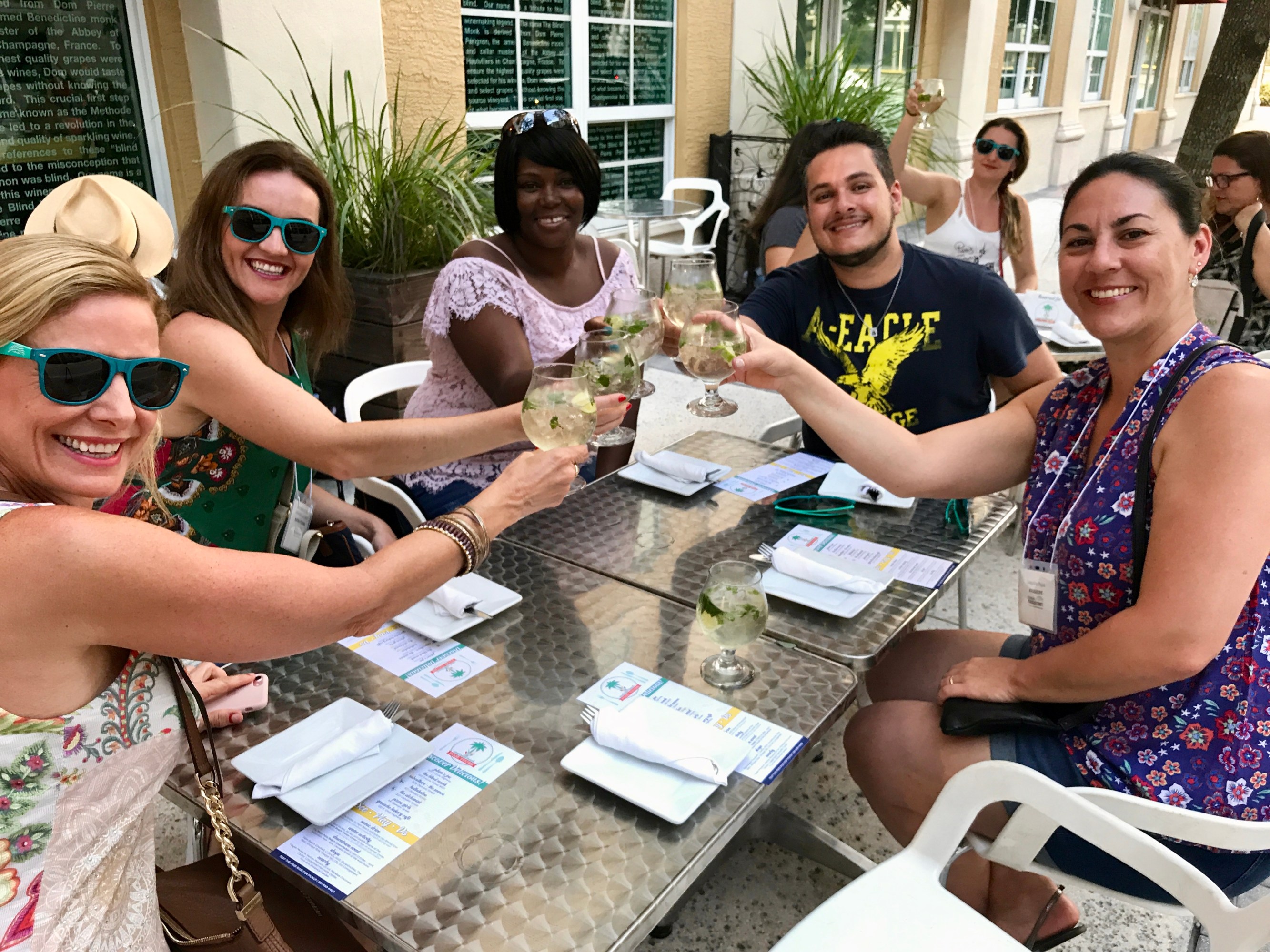 Five people toasting with drinks at an outdoor restaurant table.