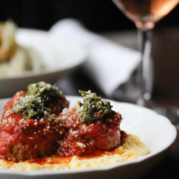 a close up of a plate of meatballs and polenta topped with pesto