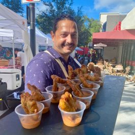 a man holding a tray of conch fritters at the west palm beach greenmarket