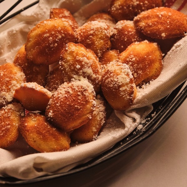 Golden madeleines dusted with powdered sugar in a lined basket.