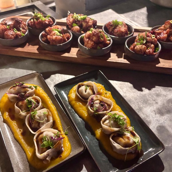 Two plates of dumplings on squash puree and small bowls of fried cauliflower on a wooden board.