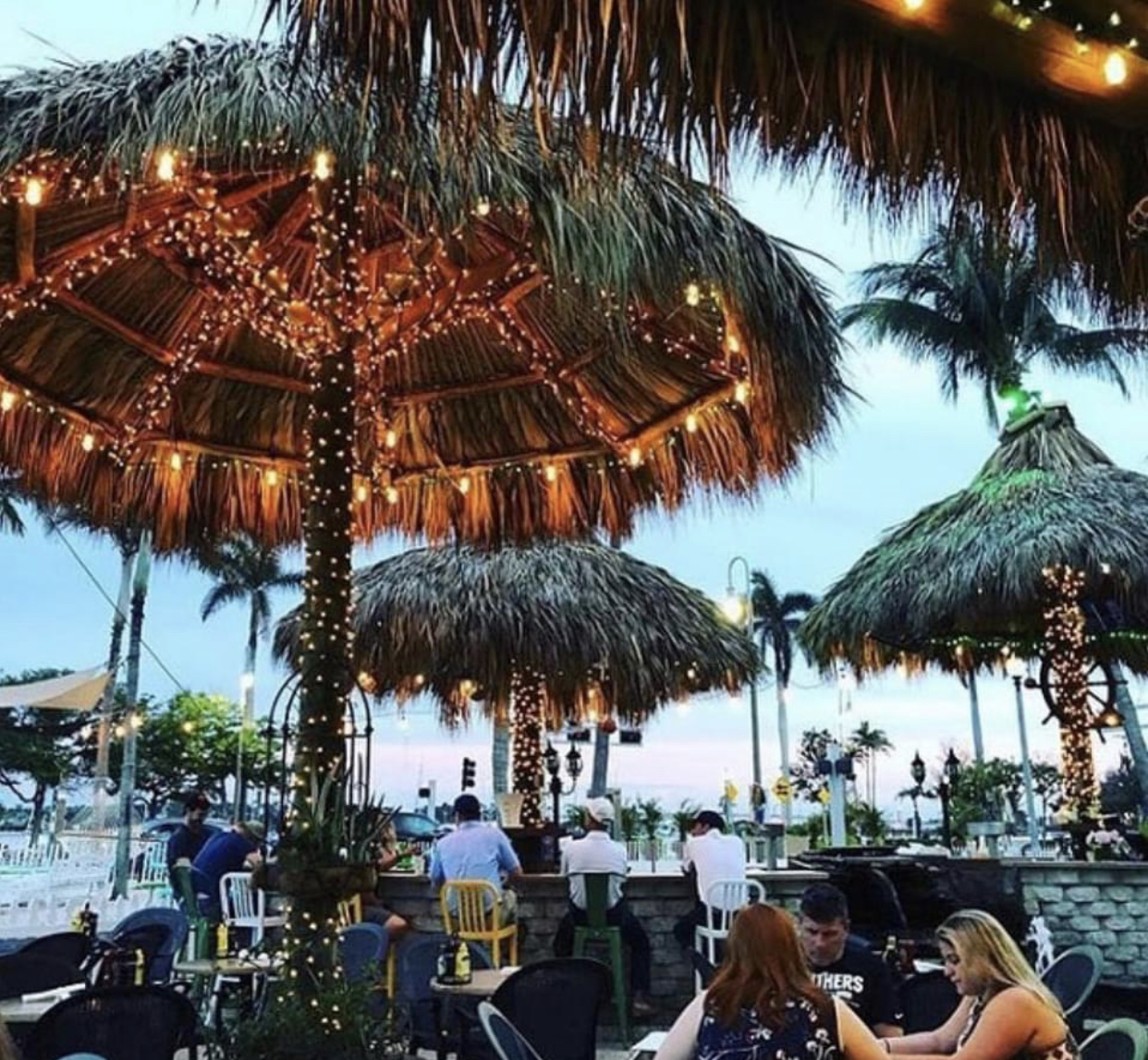 Outdoor patio with tiki huts, string lights, and people dining.
