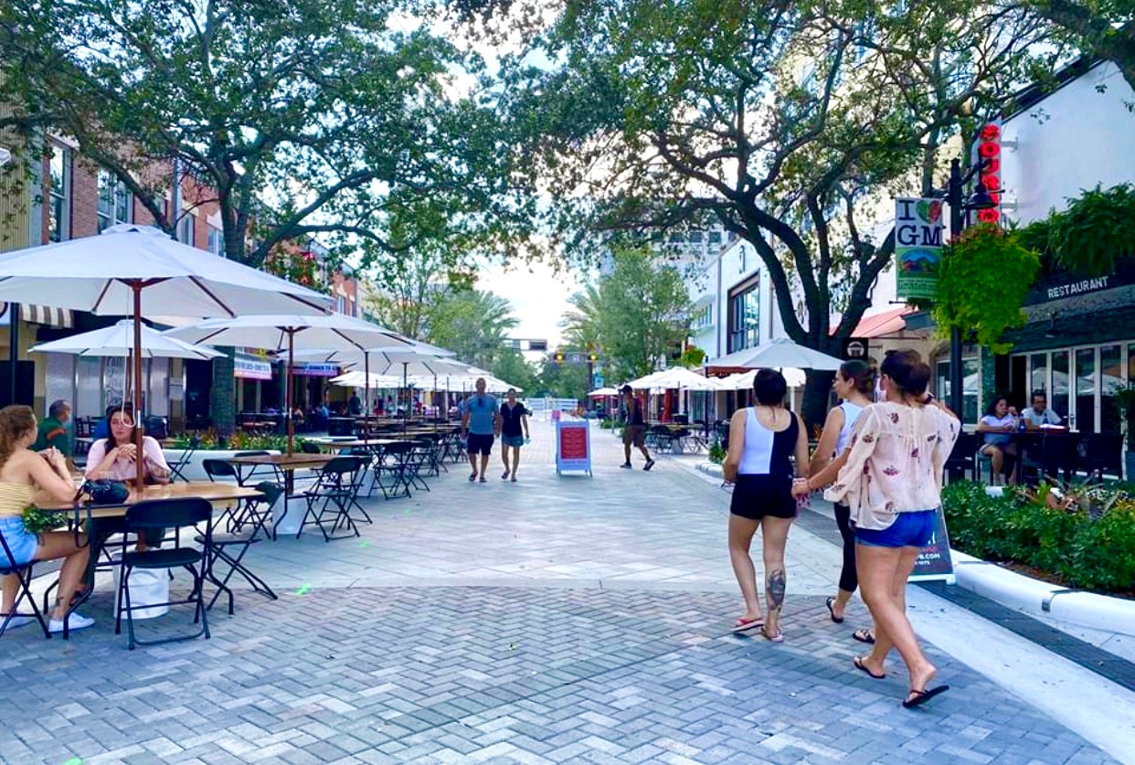 Outdoor street cafe with tables, umbrellas, and people walking.