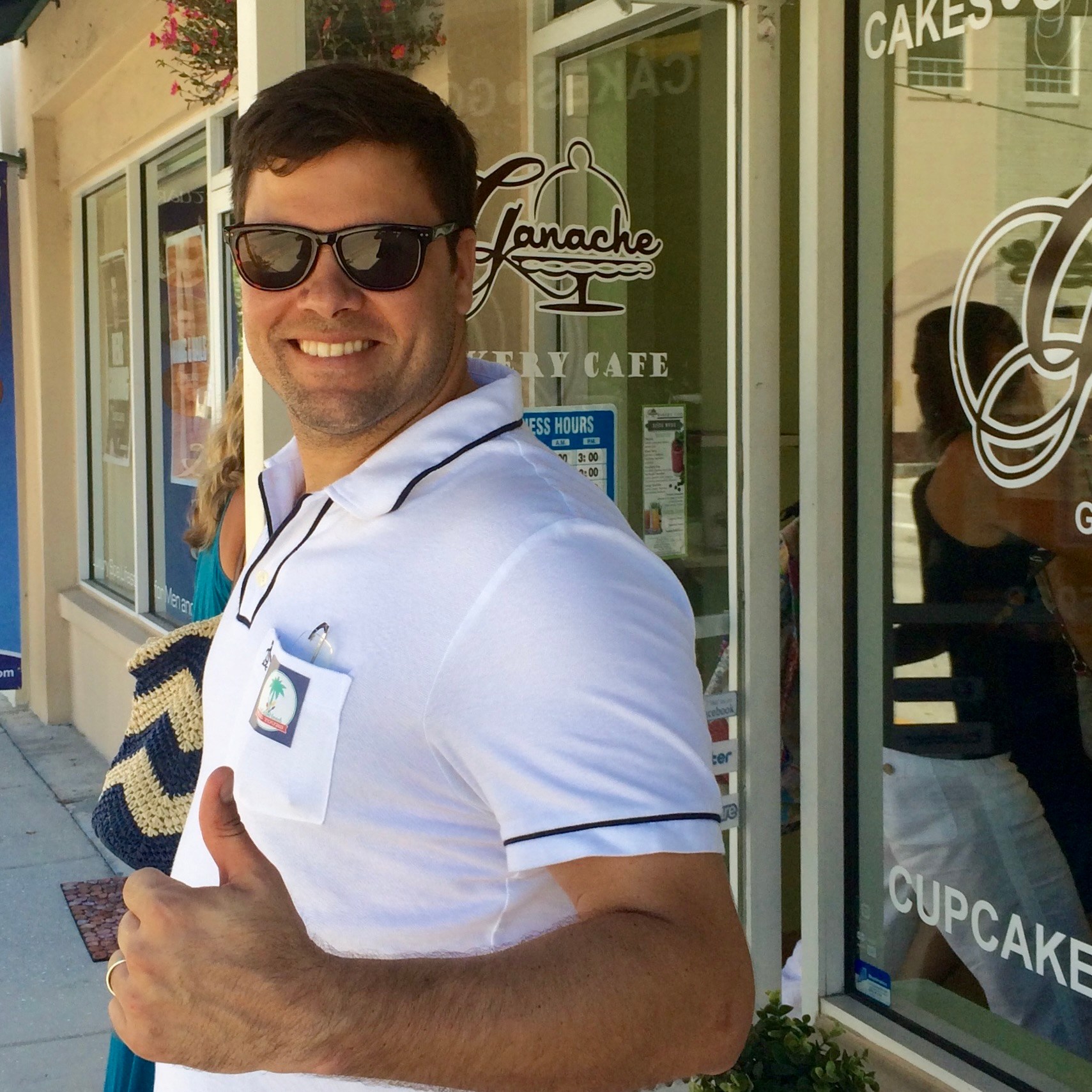 Man in sunglasses smiling and giving thumbs up outside a café.